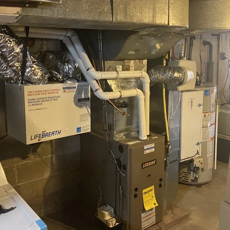 An ERV mounted beside a gas furnace in a basement, tied into the ductwork with insulated flex ducts