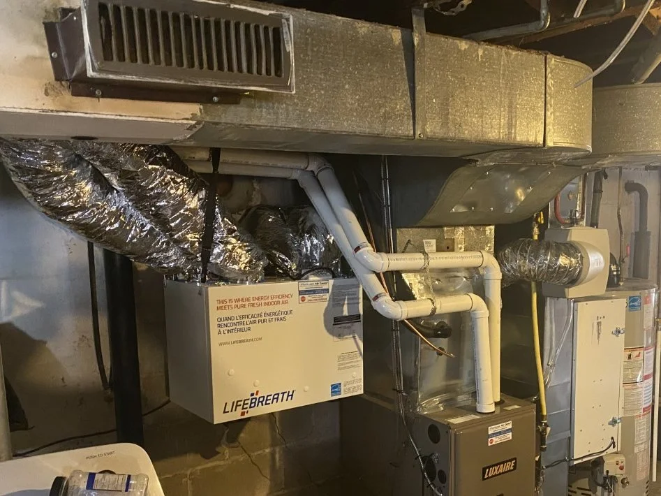 An energy recovery ventilator tied into the ductwork beside a gas furnace and a water heater in a basement