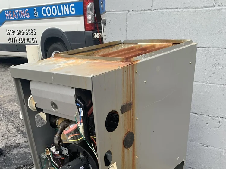 Old furnace with a rusted cabinet, set outside beside a Platinum Air Care heating and cooling van