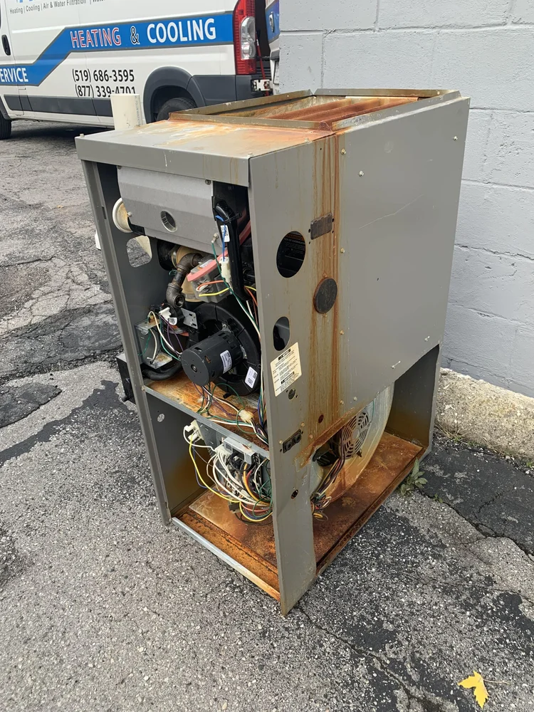 Old rusted furnace with its panel off, outside beside a Platinum Air Care heating and cooling van