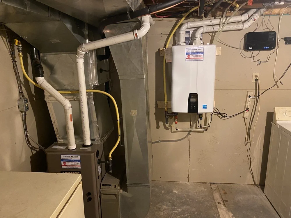 Navien tankless water heater on a basement wall beside a Luxaire gas furnace, both with Platinum Air Care service stickers