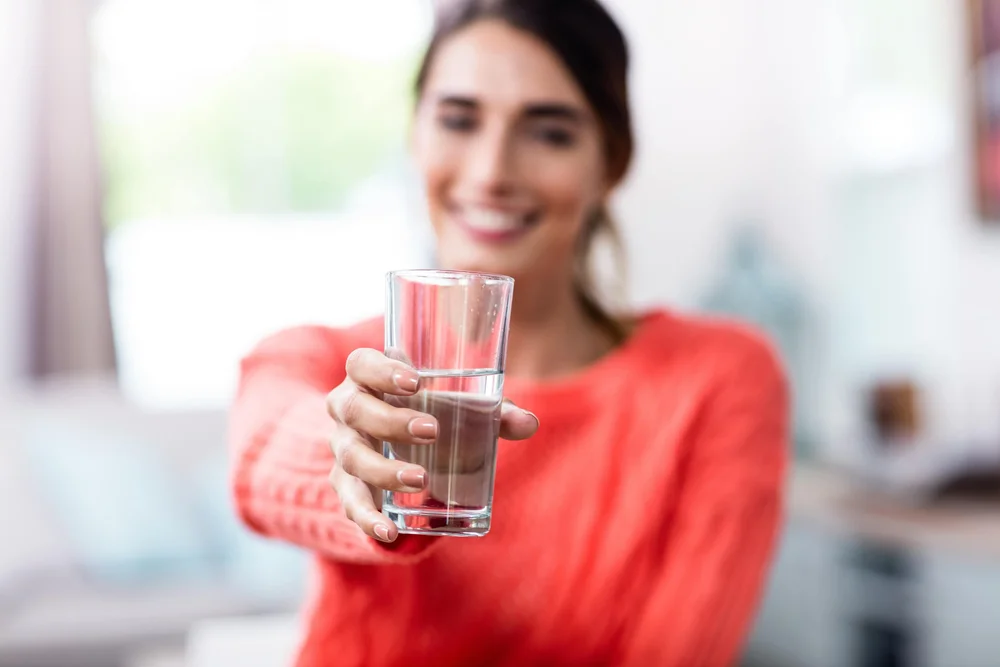 Woman smiling and holding out a glass of clean water at home