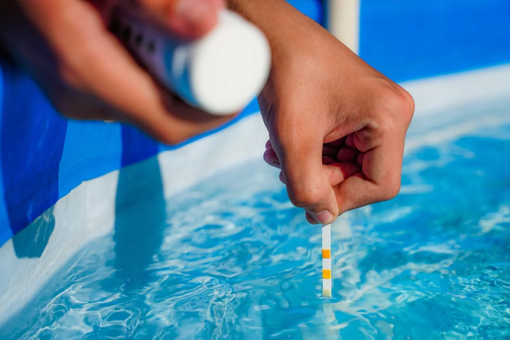 Hand dipping a chlorine test strip into blue swimming pool water