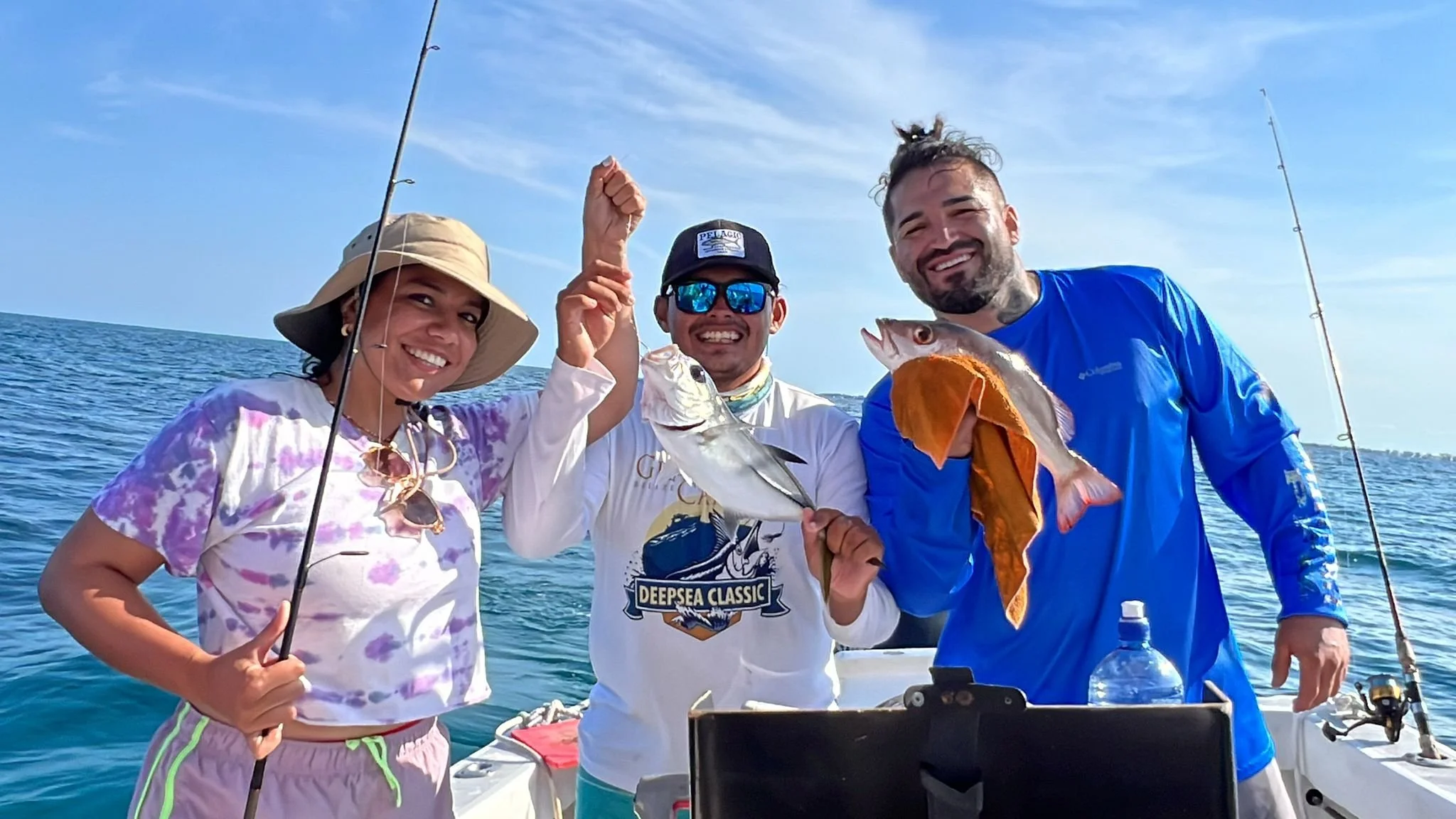 Two smiling guests and a local guide on a boat in San Pedro Belize holding up their recent catch during a sunny day of reef fishing.