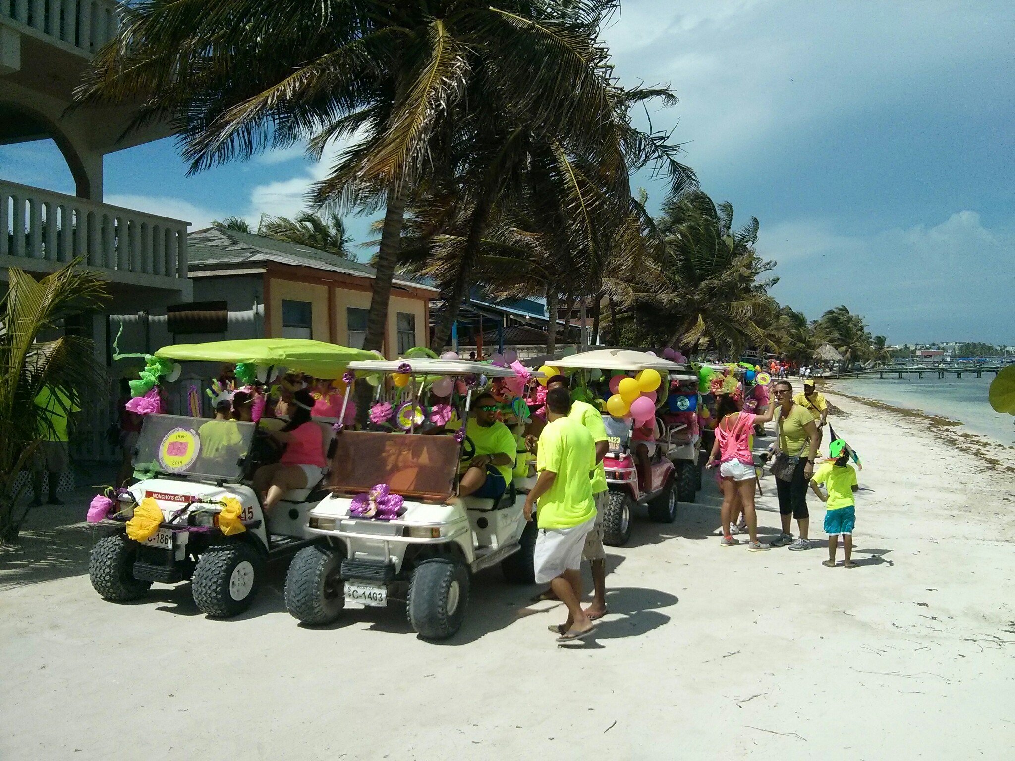 Decorated golf carts lined up along the sandy beachfront road and palm trees in San Pedro, Ambergris Caye, Belize.