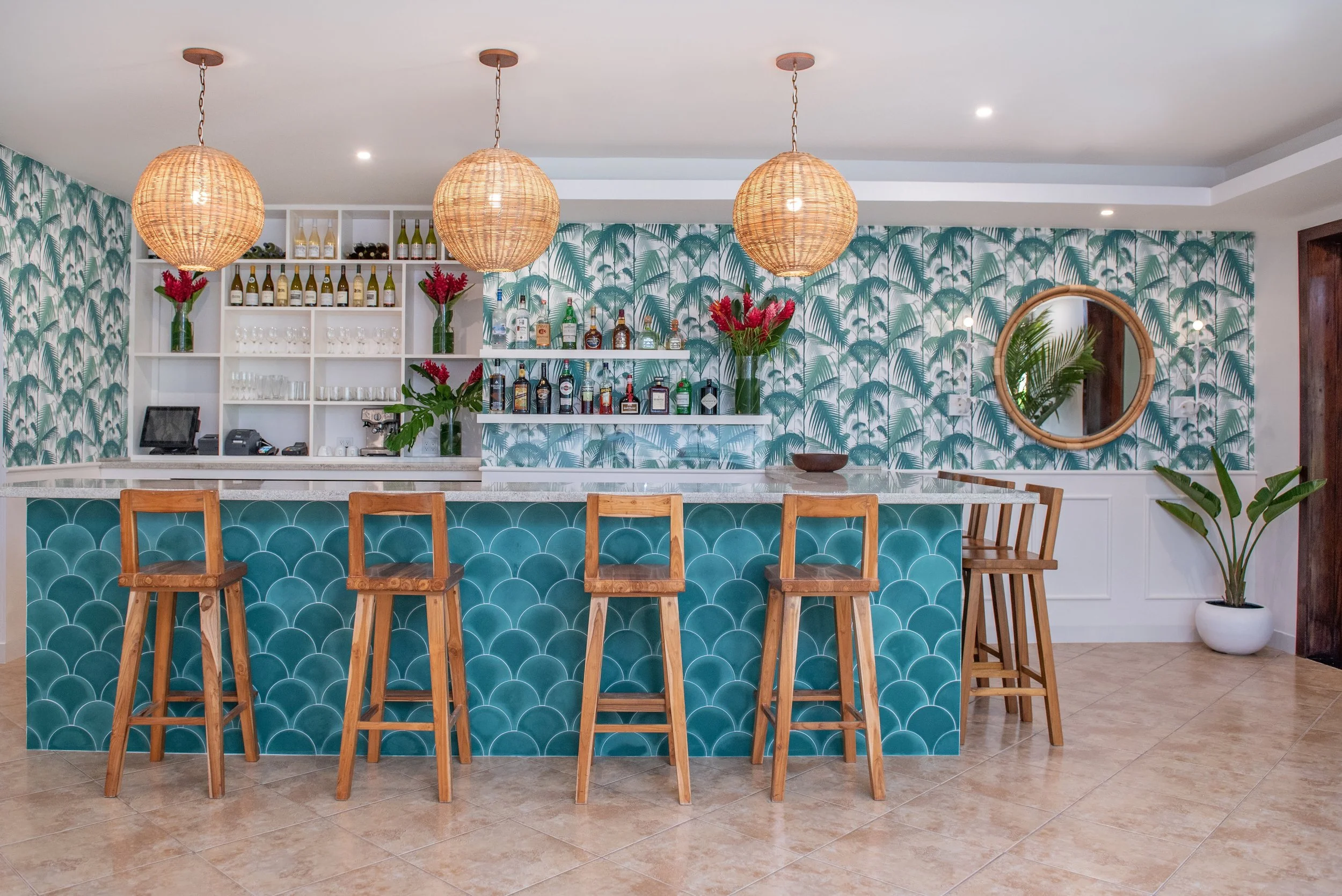 The stylish indoor bar at Red Ginger restaurant featuring teal scallop tiles, wooden barstools, woven pendant lights, and tropical palm wallpaper in San Pedro Belize.