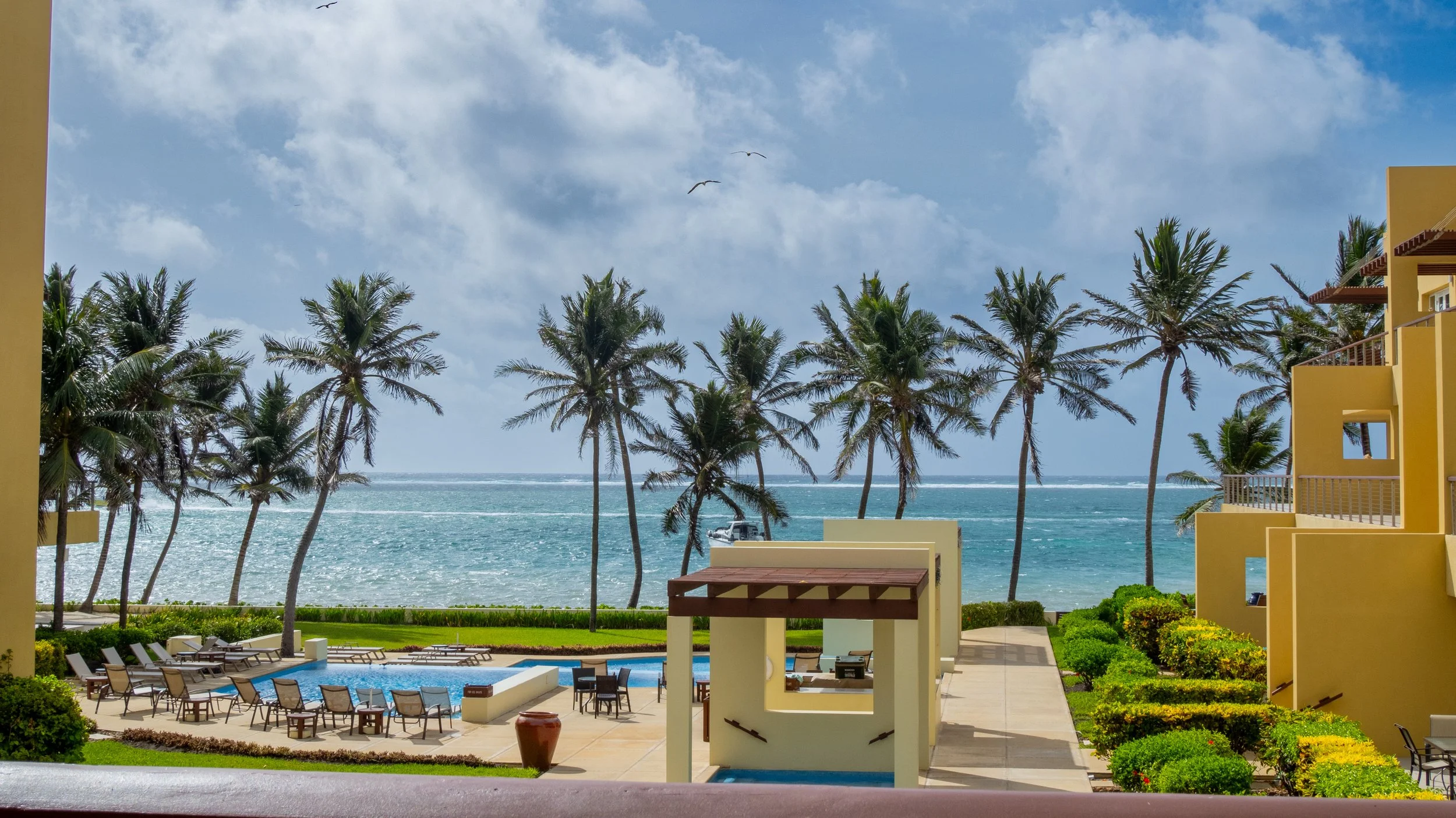 An elevated view of the swimming pools, tropical palm trees, and ocean reef view at The Phoenix Resort, a top boutique hotel in San Pedro Belize.