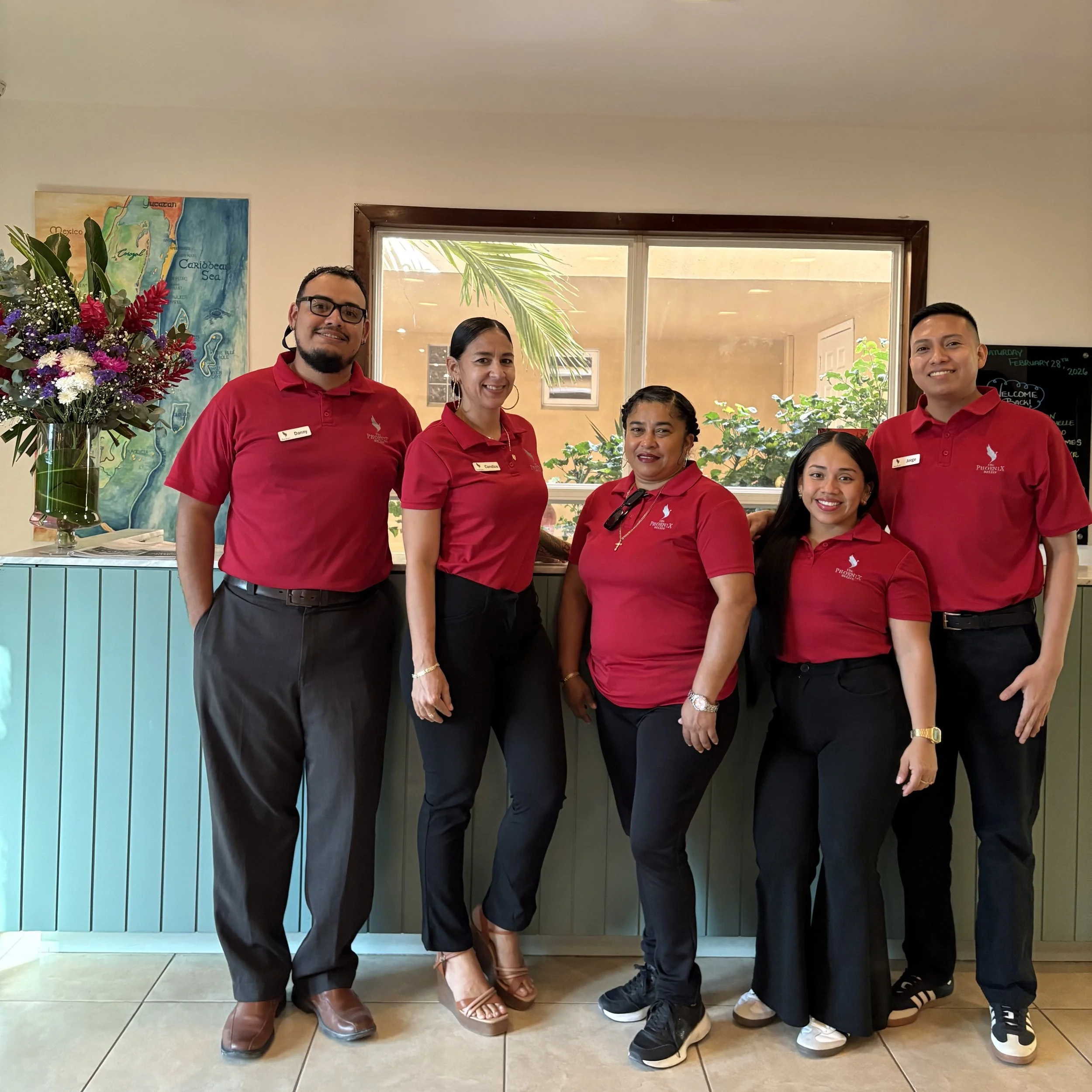 The welcoming guest services and reception team standing at the front desk of The Phoenix Resort in San Pedro, Belize.