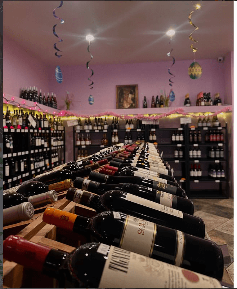 Interior of Wine de Vine in San Pedro featuring floor-to-ceiling wooden wine racks filled with imported bottles.