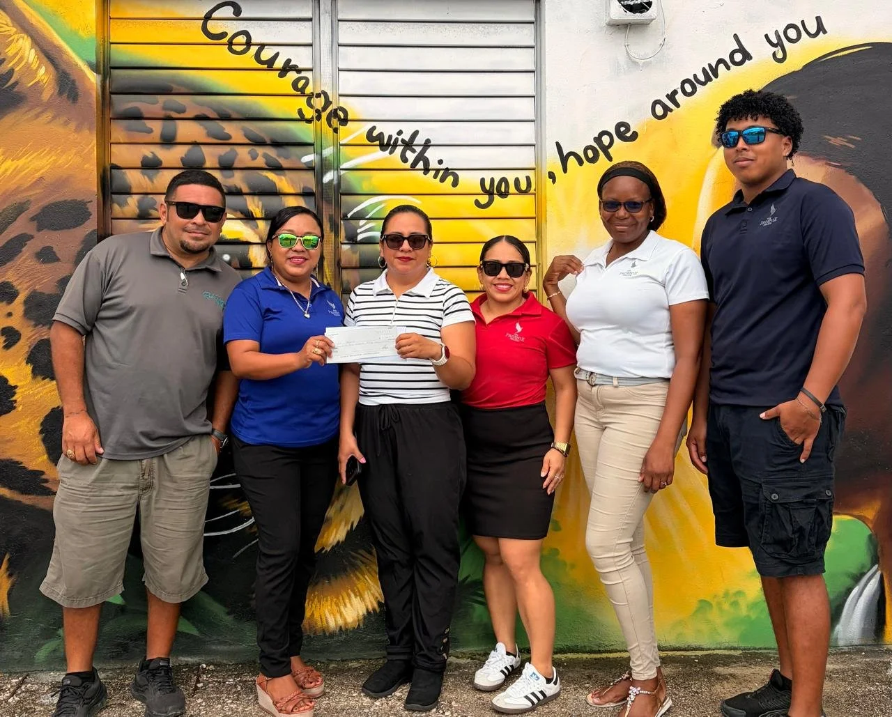 The Phoenix Resort team presenting a charitable donation check to representatives of Hope Haven San Pedro in front of a colorful community mural.