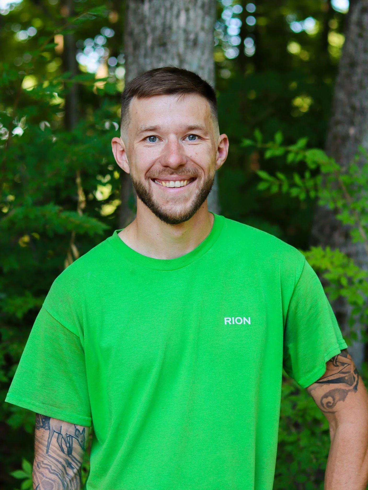 Smiling man in green t-shirt standing by an open car door outdoors.