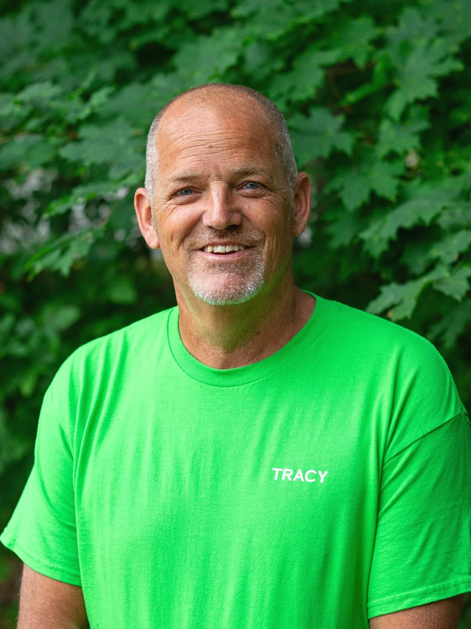 Man wearing a green shirt and a black "Mountain Deer" cap outdoors.