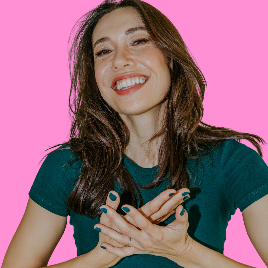 Photo of Amy smiling with her hands over her heart in front of a bright pink background