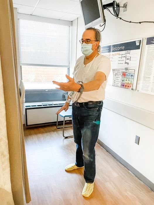 一名身穿t恤和牛仔裤的男子在医院病房里打太极，脖子上挂着一个吊雷竞技reybat客服电话带监视器。