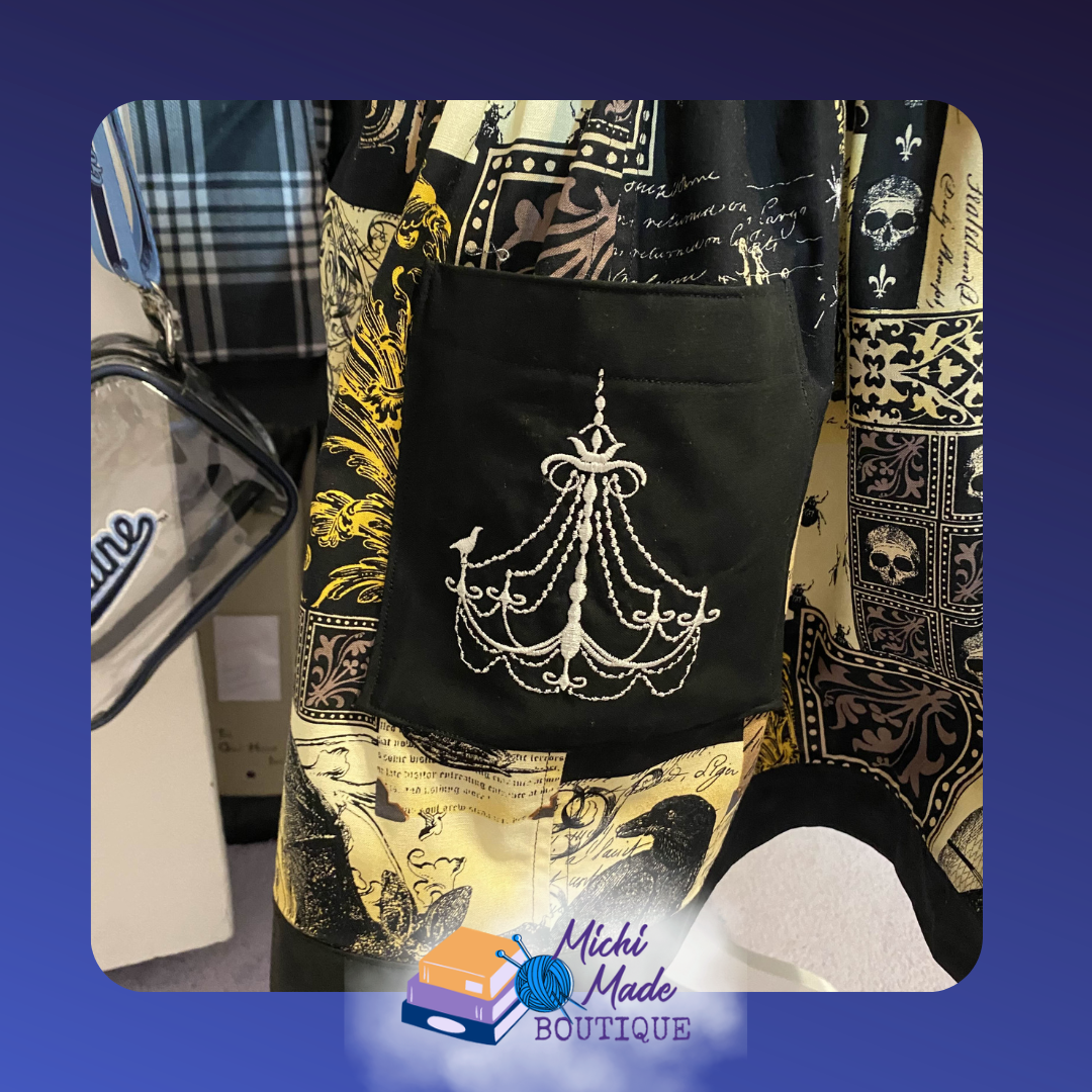 Apothecary_Pocket.png Close-up of a black apron pocket embroidered with a white chandelier with draping crystals and a small raven perched on one arm.