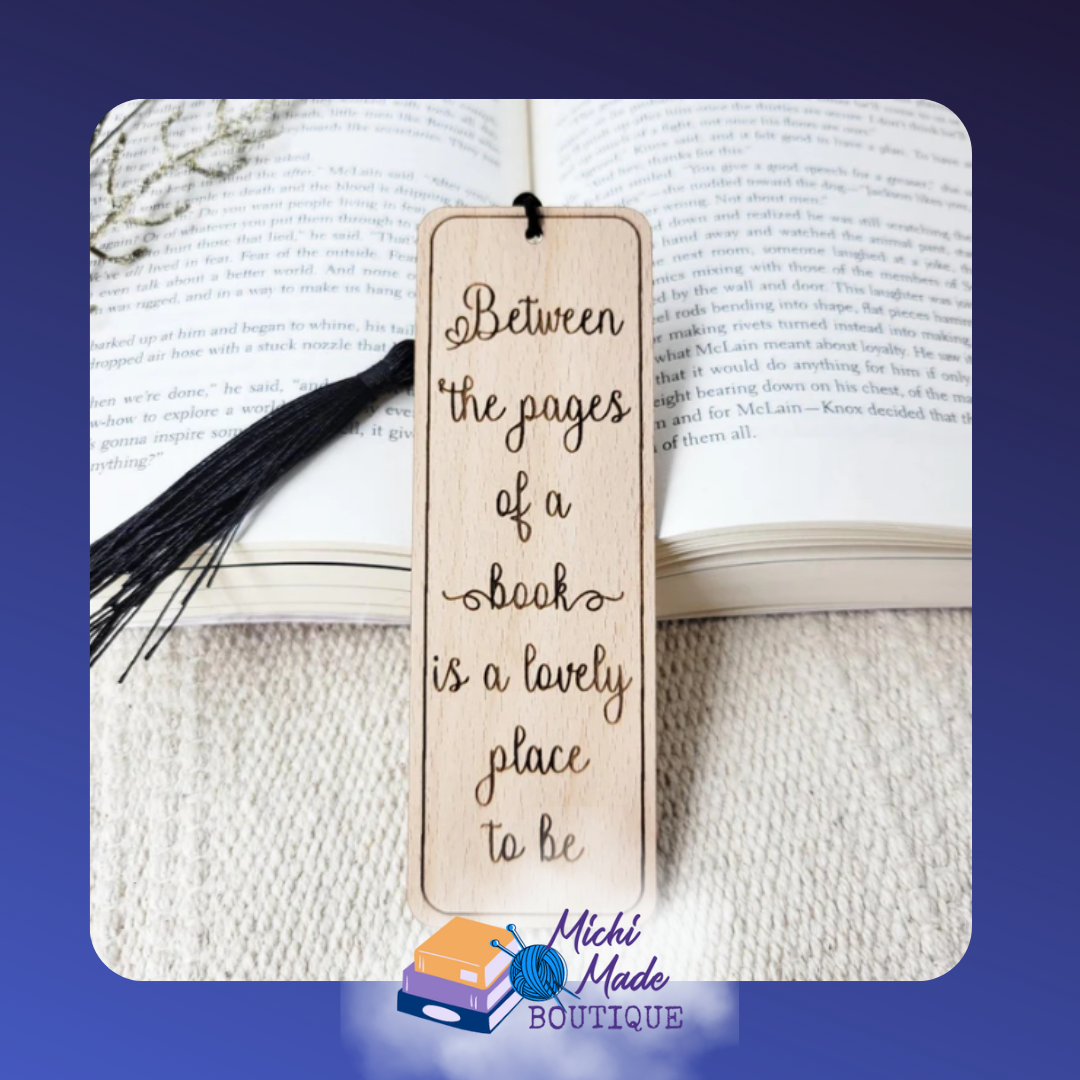 Wooden bookmark engraved with "Between the pages of a book is a lovely place to be," with black tassel.