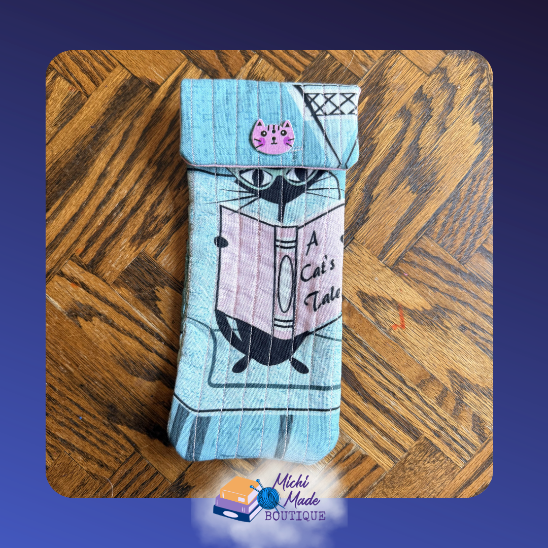 Retro Cat & Book Eyeglass Case.png Quilted eyeglass case in teal with a retro black cat reading A Cat's Tale, pink panel accent, and pink cat face button with rosy cheeks.