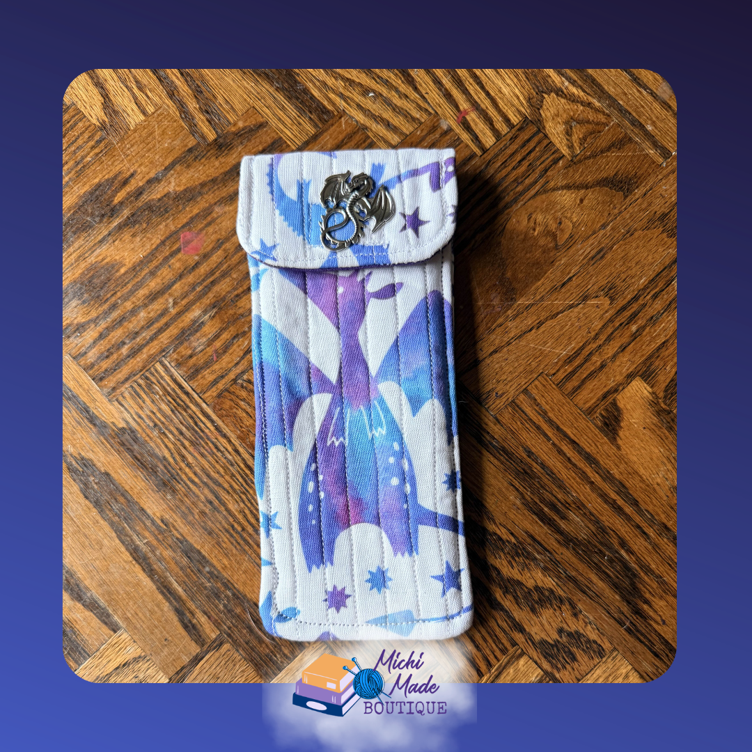 Dragon Flight Ice & Sky. Quilted eyeglass case in white with watercolor blue and purple dragon wing silhouettes and star motifs, fastened by a small silver winged dragon decorative button.