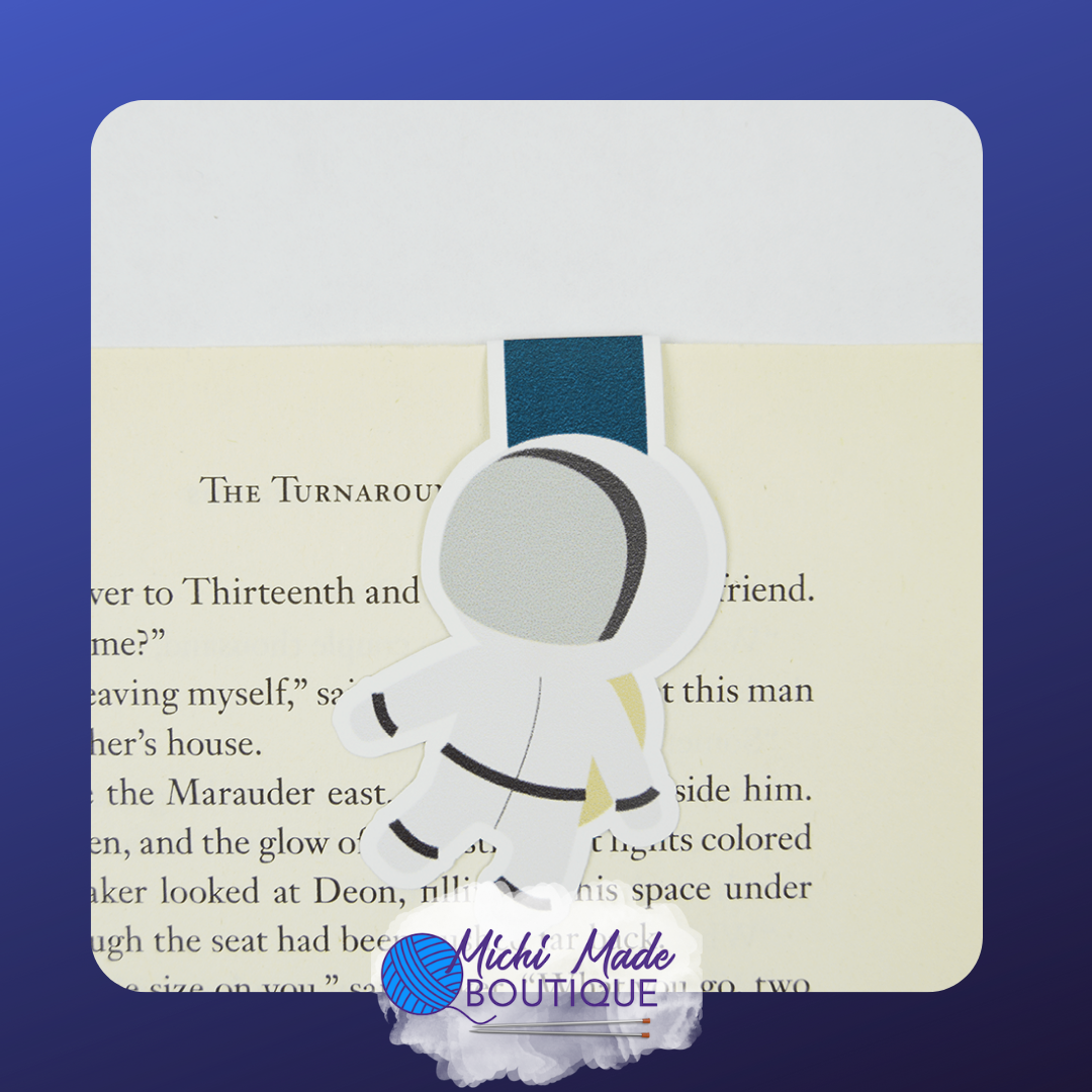 Astronaut-shaped magnetic bookmark holding a page, featuring a white suit and dark visor.