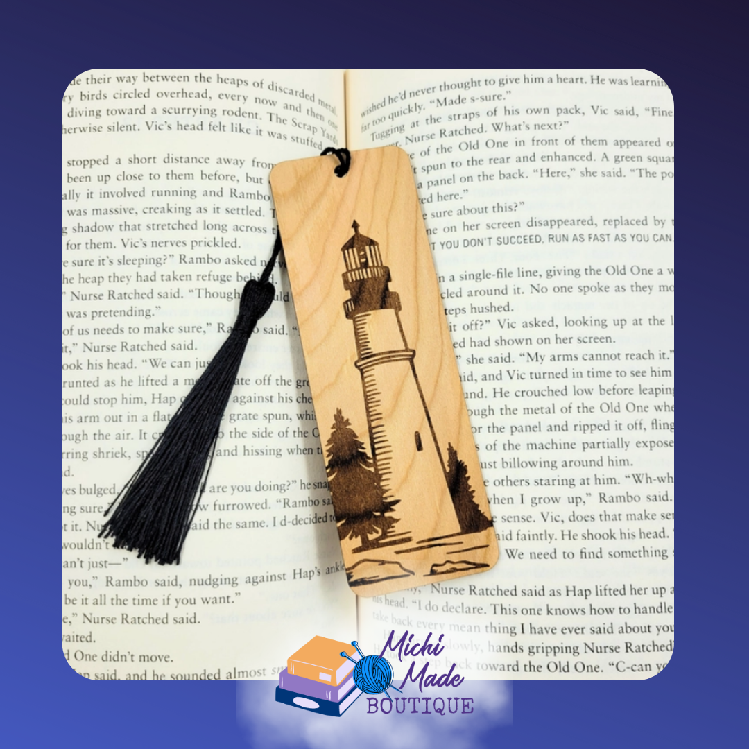 Wooden bookmark with engraved lighthouse and pine trees, black tassel attached.