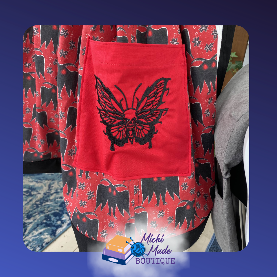 Mothman_Pocket.png Close-up of a red apron pocket embroidered with a detailed black skull moth with wide-spread wings and a skull face at its center.