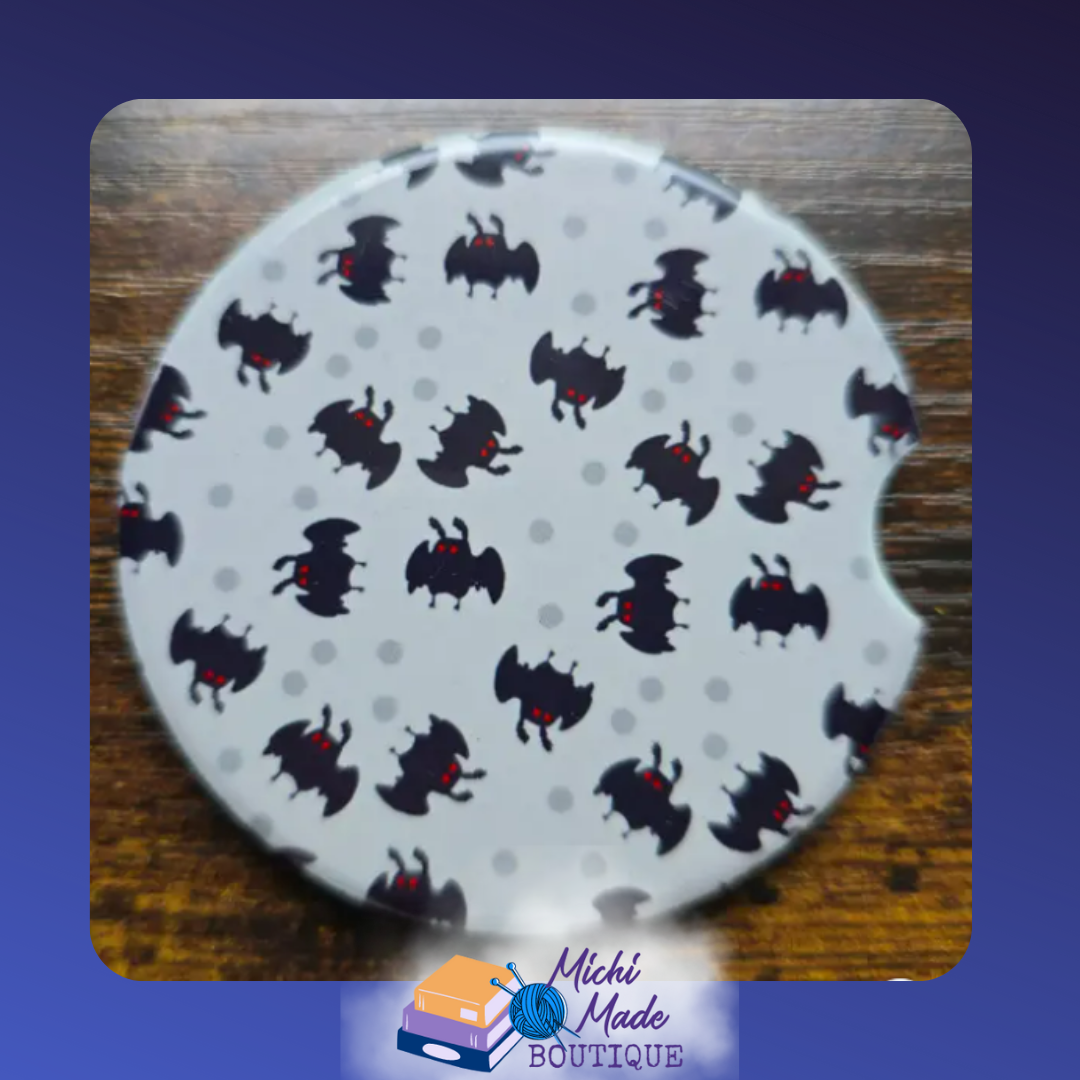 Ceramic car coaster with repeating cartoon Mothman pattern on a light gray dotted background.