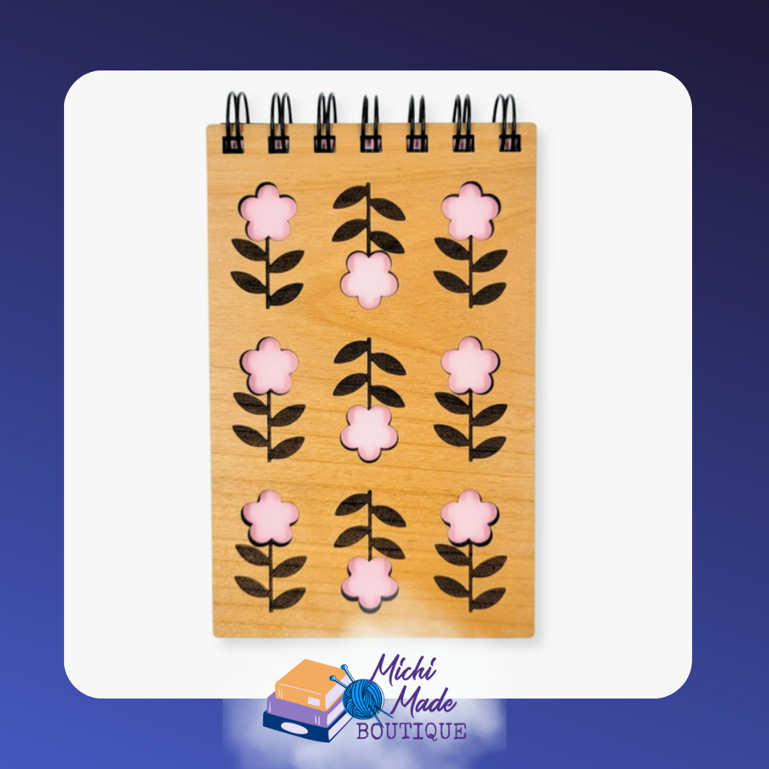 Small wood-cover notepad with pink flower cutouts in a repeating pattern.