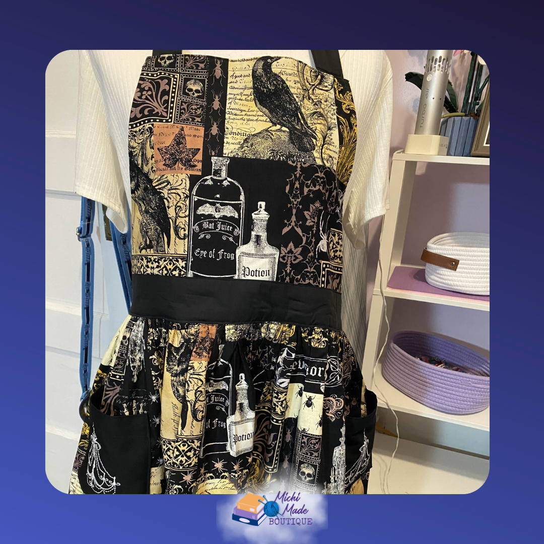 Apothecary_1.png Gothic apron bib on a dress form featuring black and gold fabric with ravens, potion bottles, skulls, and aged manuscript print, with a wide black waistband and full gathered skirt.