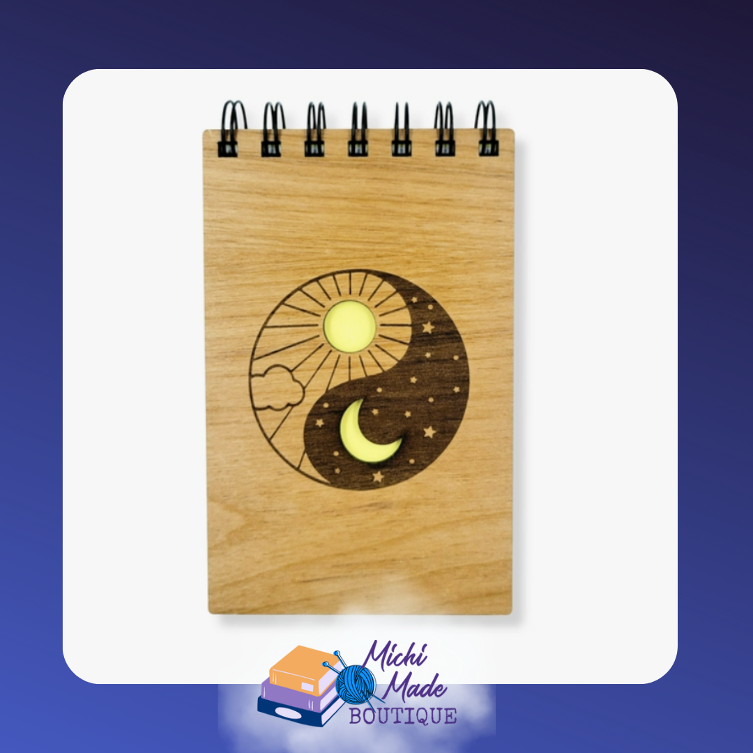 Small wood-cover notepad engraved with yin yang sun, moon, clouds, and stars.