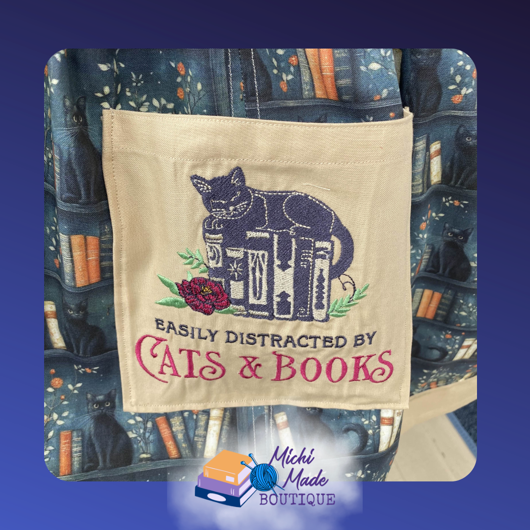 Easily Distracted By Cats and Books Pocket.png Cream apron pocket embroidered with a black cat on stacked books, a red peony, and the text Easily Distracted by Cats and Books.