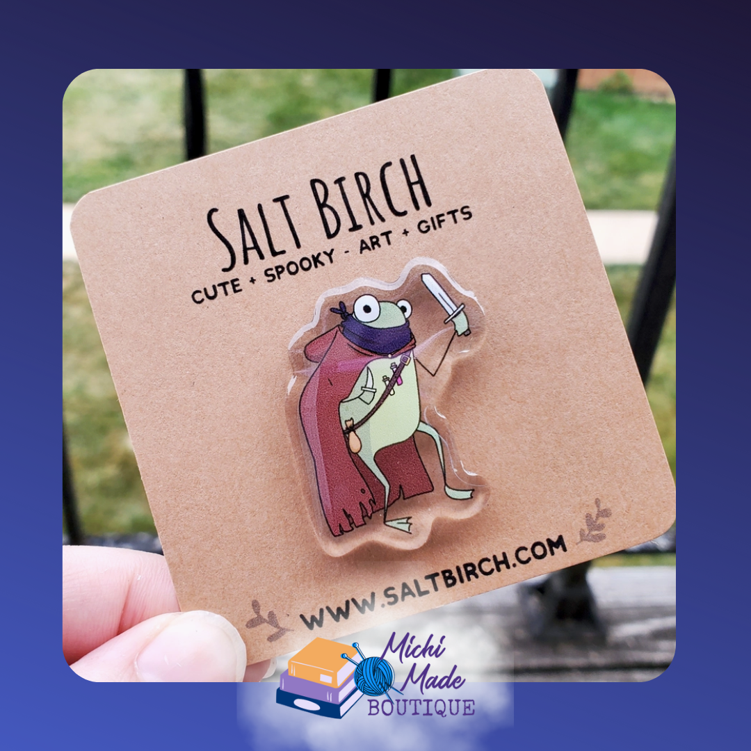 Acrylic pin of rogue frog in purple cape holding dagger and wearing a brown cape.