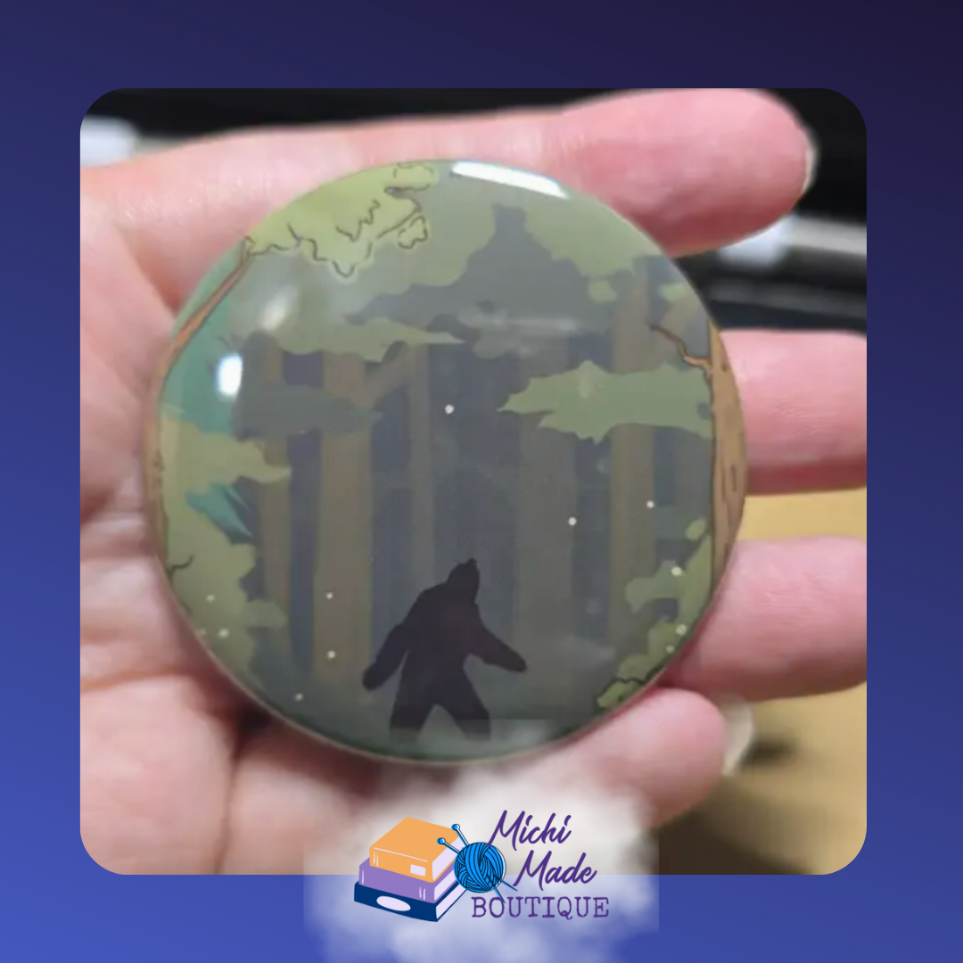Bigfoot Sasquatch Fridge Magnet – Cartoon Bigfoot holding a lantern, standing among pine trees on a round magnet.