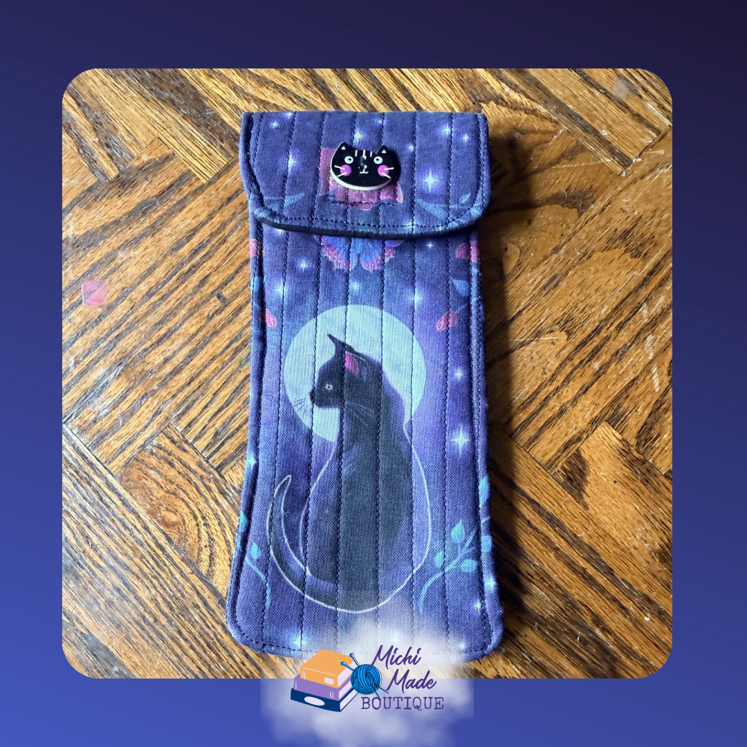 Midnight Cat. Quilted eyeglass case in deep purple with a black cat against a glowing full moon, sparkles, and pink butterfly motifs, fastened by a cat face decorative button with pink cheeks.