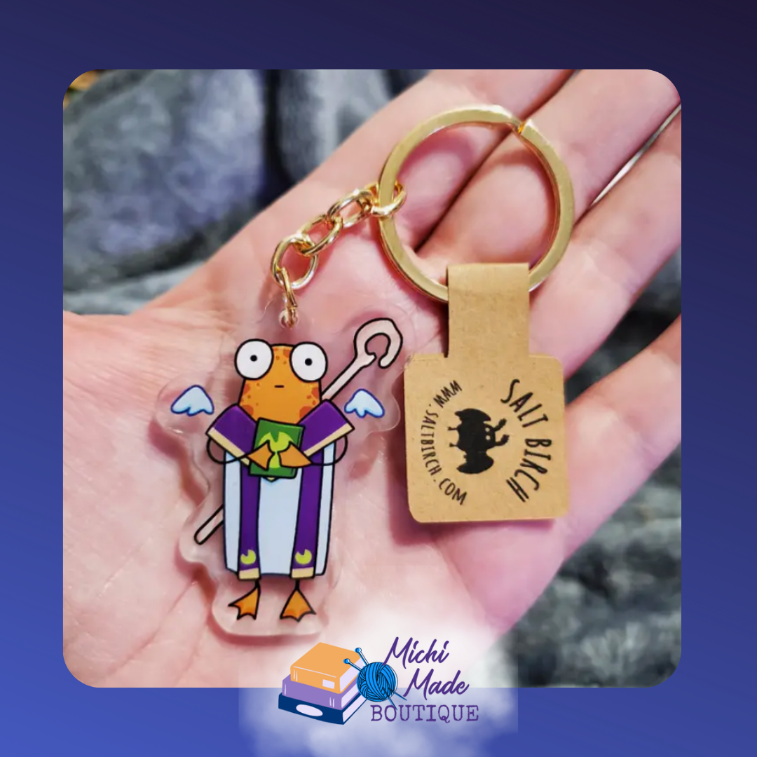 Priest frog keychain in purple robes holding green book.