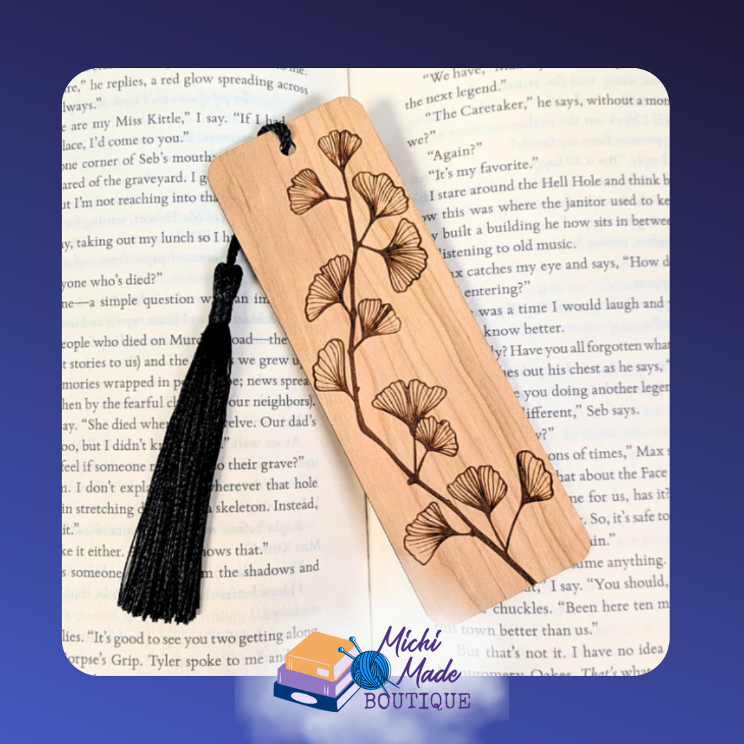 Wooden bookmark with engraved gingko leaves along the length, black tassel, on open book.