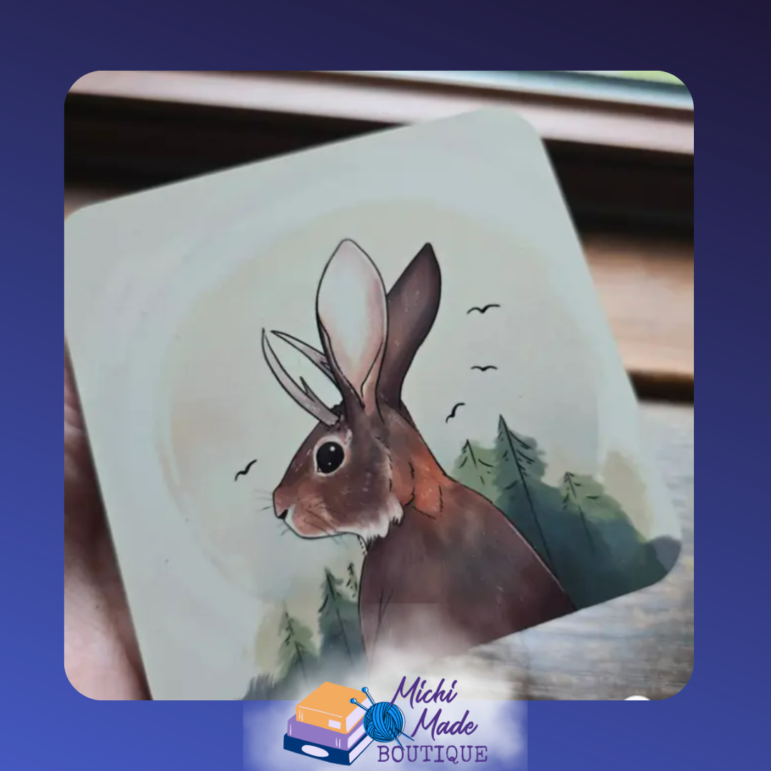 Illustrated coaster of a brown jackalope with tall ears and antlers in front of pine trees.