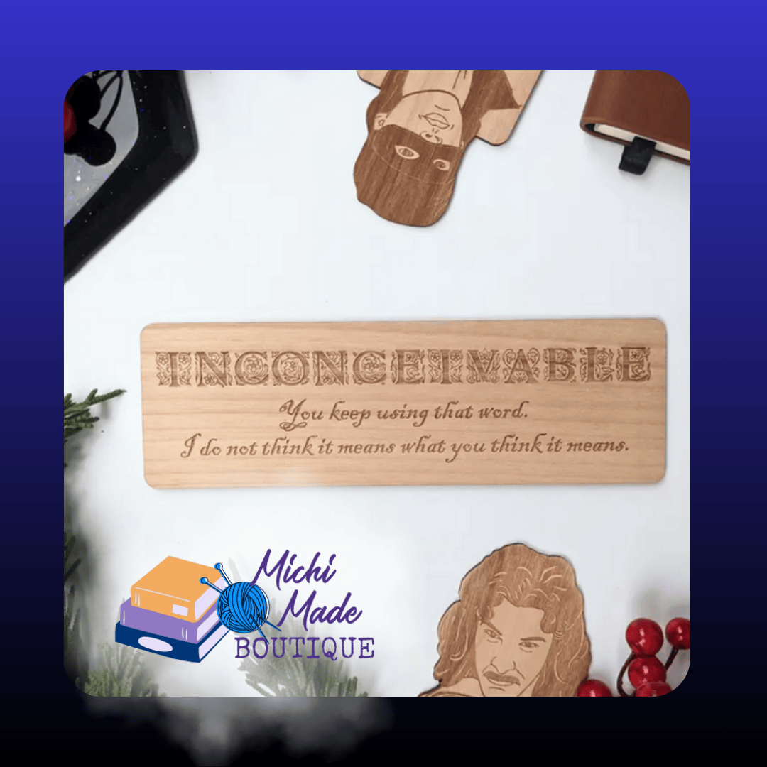 Flat lay: “Laser-engraved alder wood bookmark reading ‘Inconceivable’ with the quote beneath, displayed on a white background with dice and greenery.”