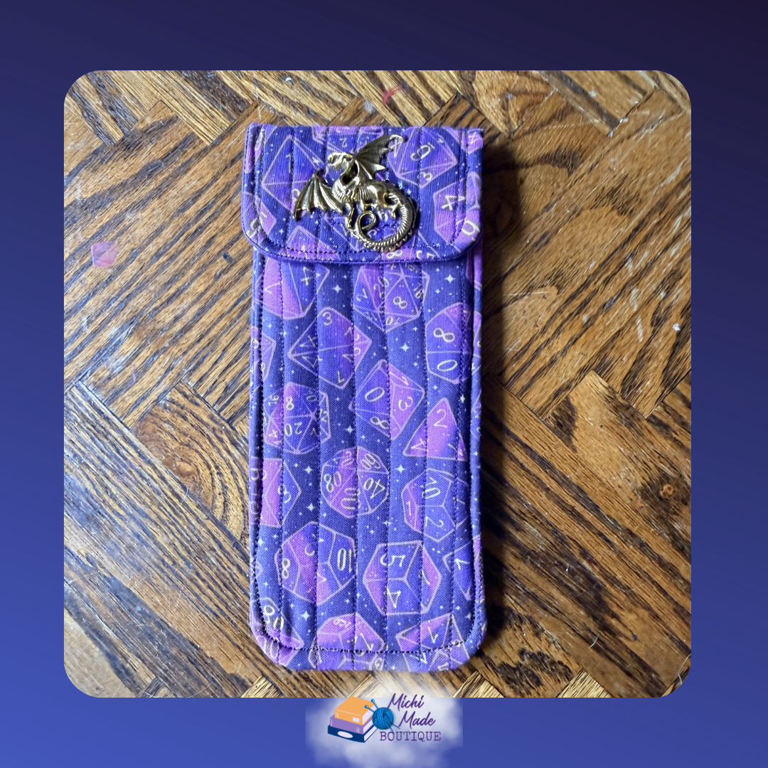 Dice Dragon Arcane Purple. Quilted eyeglass case in vivid purple with pink and white polyhedral dice and stars, fastened by a bronze winged dragon decorative button.