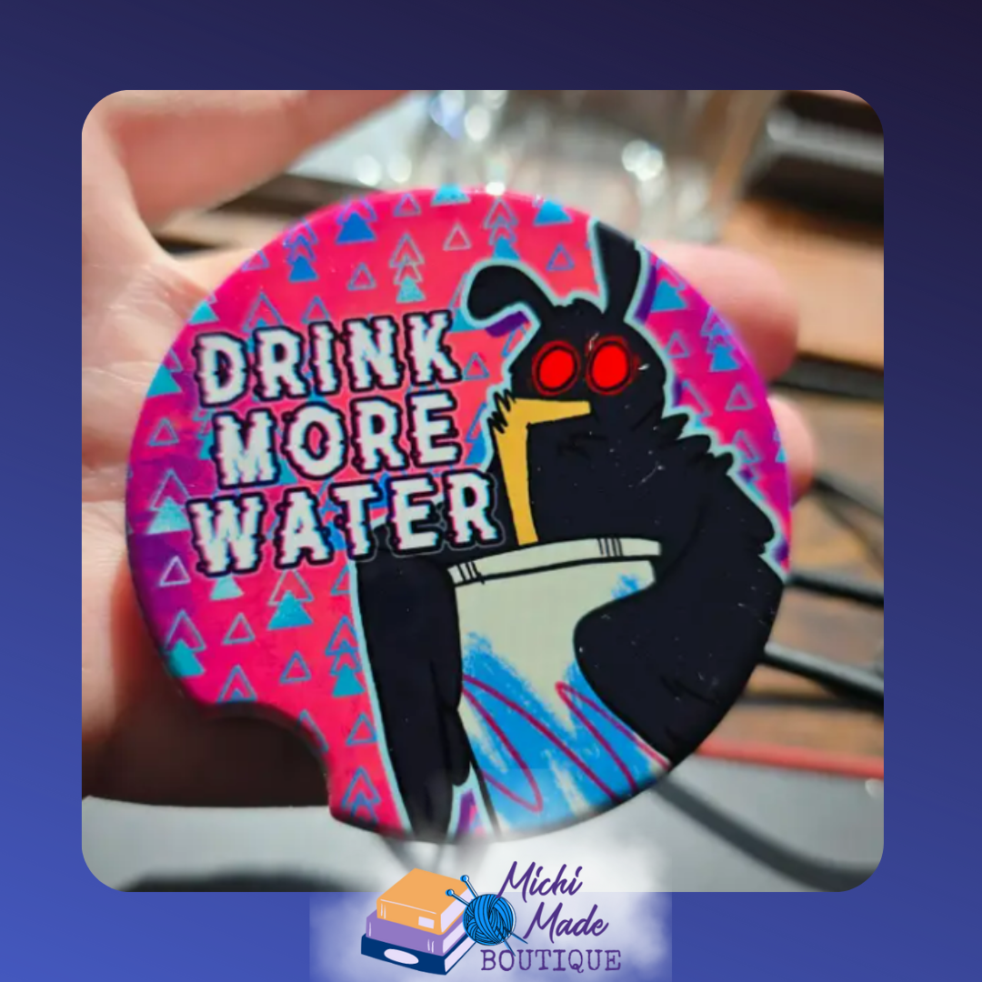 Ceramic car coaster with cartoon Mothman holding a drink and text “Drink More Water” on a colorful background.