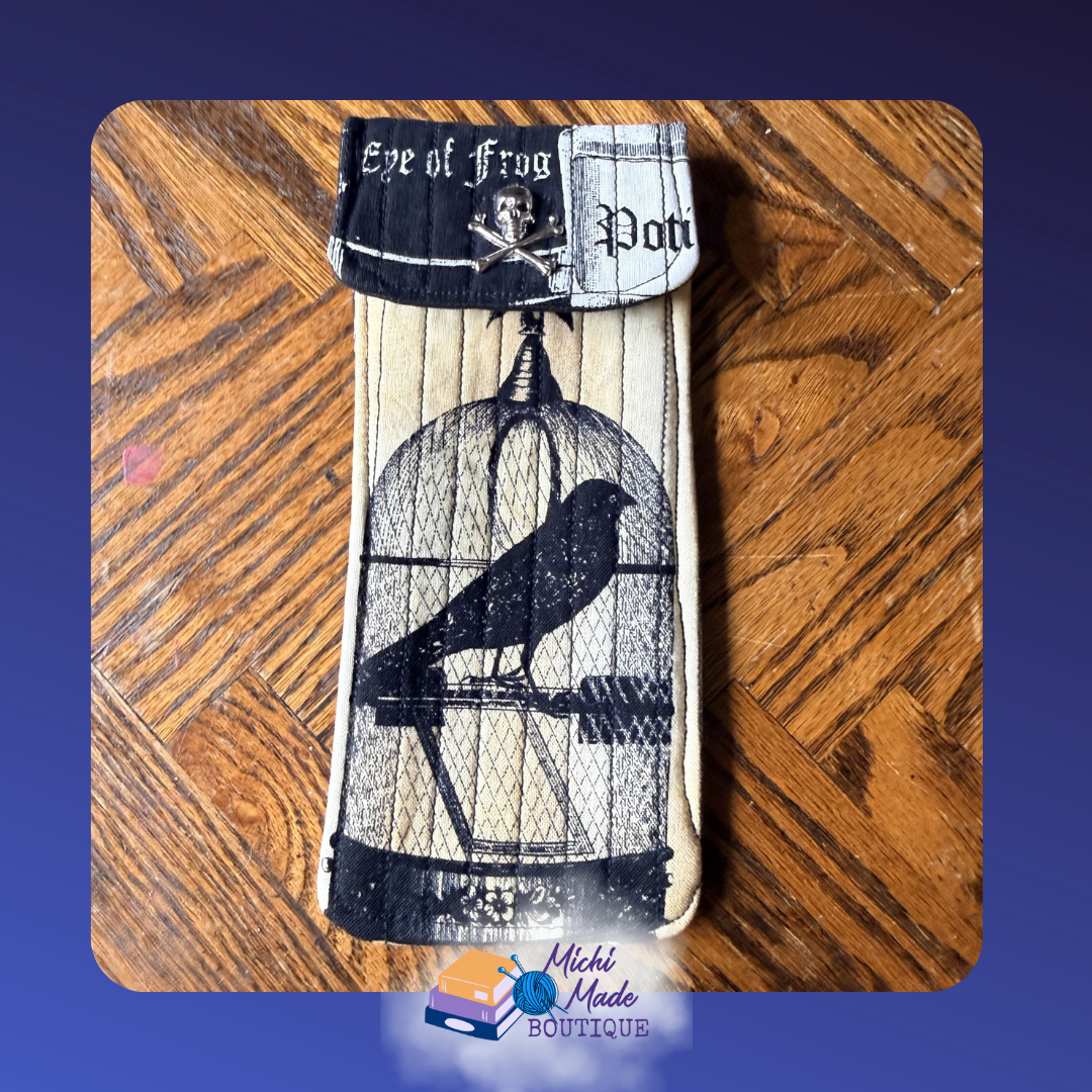 Gothic Crow Case.png Quilted eyeglass case in aged cream with a black crow in a domed birdcage, gothic apothecary text on the flap, and skull and crossbones button.