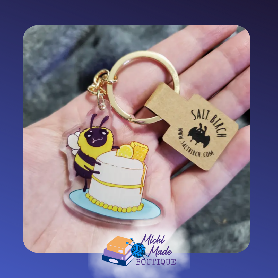 Cute bee keychain holding lemon cake with honeycomb.