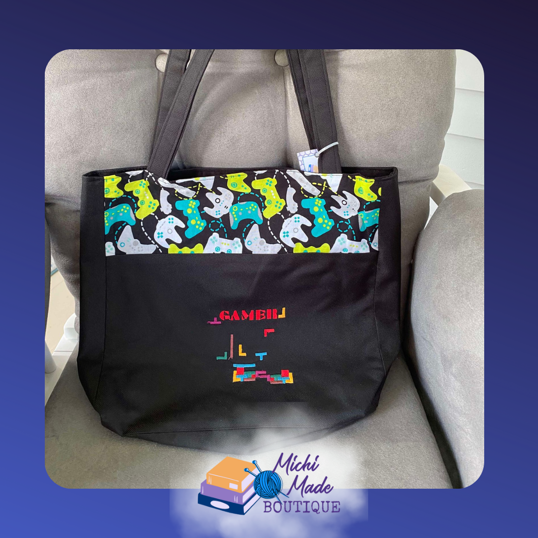 Gamer Black Embroidered Tote Bag.png Black tote bag with colorful game controller print fabric panel and GAMER embroidered in pixel lettering above falling Tetris block pieces on the front.