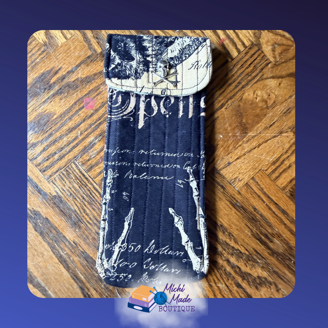 Gothic Skeleton Case.png Quilted eyeglass case in black with white script and skeleton hands, cream and black patchwork flap, and silver skull and crossbones button.