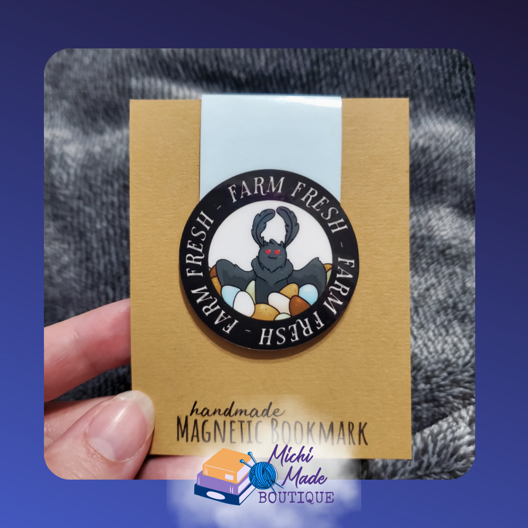 Cute Mothman holding a wooden farm produce crate. The words Farm Fresh appear three times in a circle around the mothman. White print on Black circle.