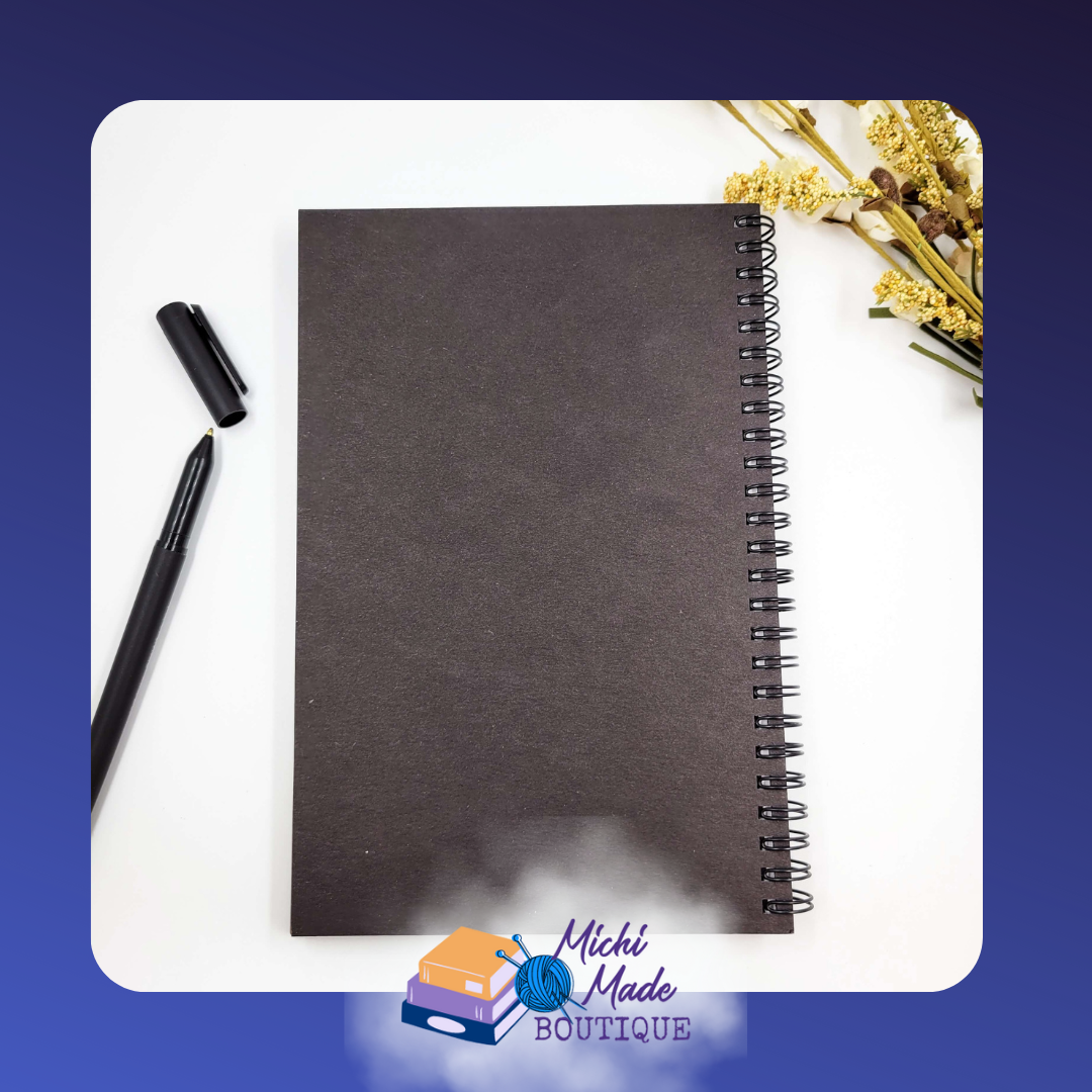 Black Journal Back Cover – Solid black back cover of spiral-bound wood journal with pen and yellow flowers beside it.