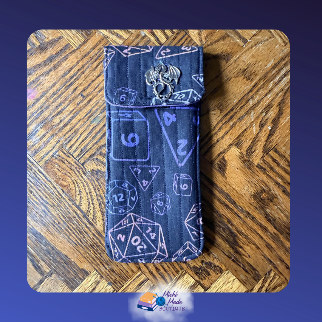 Dice Dragon Midnight. Quilted eyeglass case in black with purple and lilac polyhedral dice outline print including D20s and multi-sided shapes, fastened by a silver winged dragon decorative button.