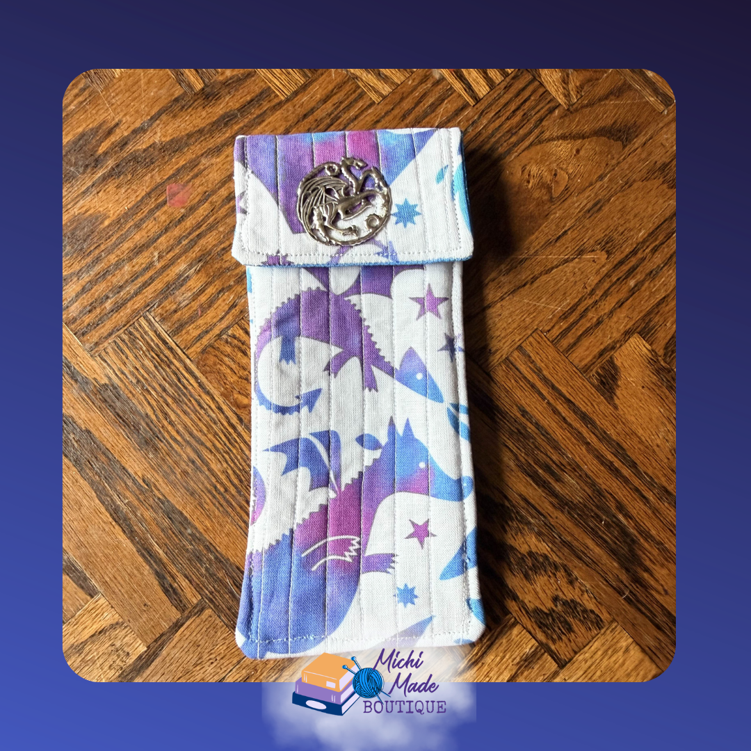 Dragon Flight Twilight. Quilted eyeglass case in white with large bold purple and blue dragon silhouettes and stars, fastened by a round silver dragon medallion decorative button.