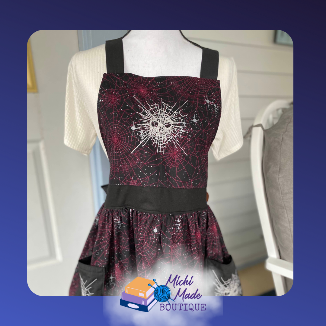 Galactic Spiderwebs apron: Deep purple and black apron with pockets with a spiderweb style mask embroidered on the bib. Side pockets are embroidered with spiderwebs as well.