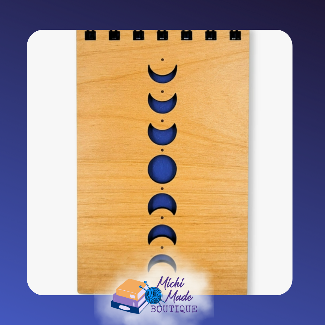 Small wood-cover notepad with vertical moon phase cutouts over deep blue.