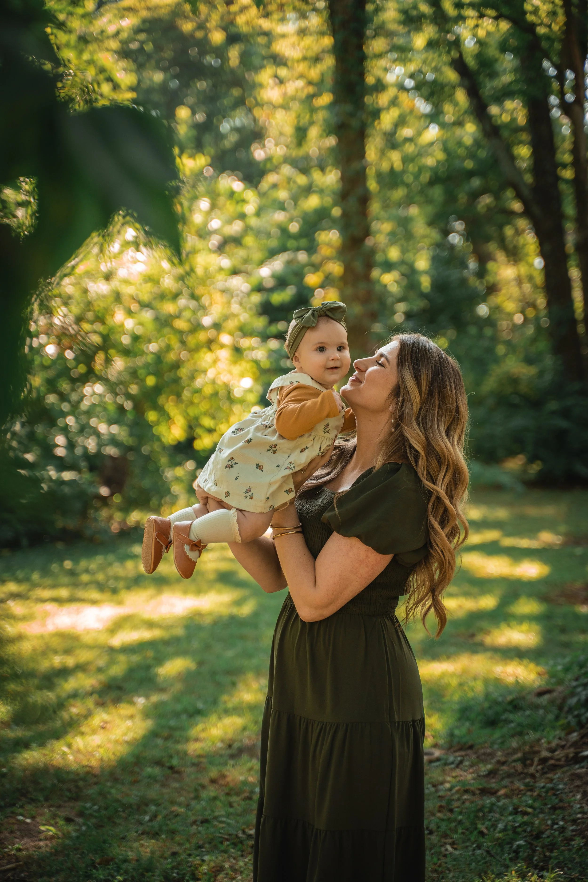 Mother lifting her baby in a sunlit forest